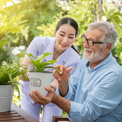 caregiver assisting elderly male resident with potting plants